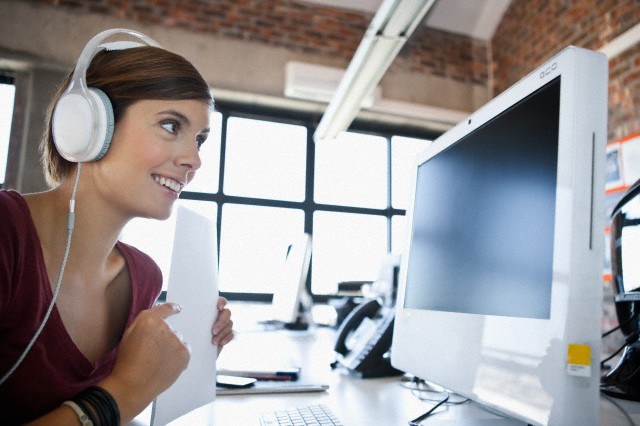 Mujer joven trabajando en la computadora y escuchando música en la oficina